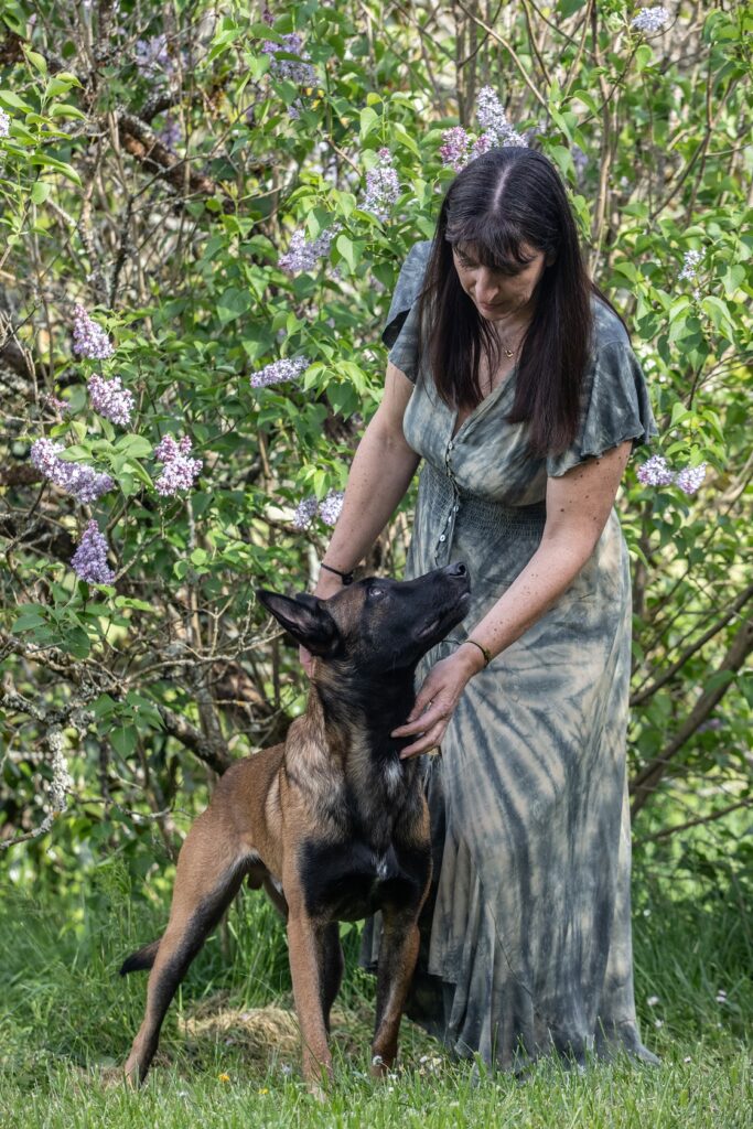 Cécile Granger en robe verte caressant Tao, son chien berger belge malinois, devant un lilas en fleurs pour la page d'accueil du site La voix des chiens - Comprendre et éduquer son chien